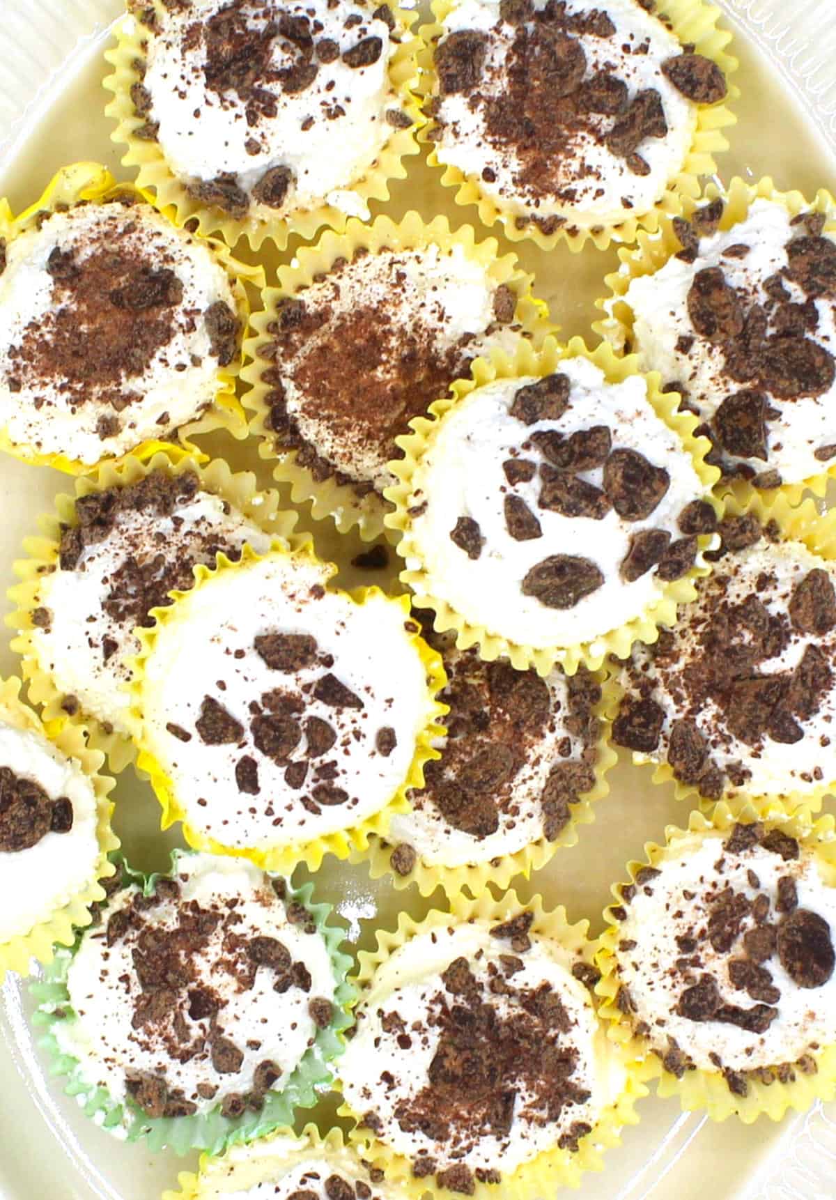 Mini vegan keto cheesecake bites in yellow and green muffin liners with chocolate bits.