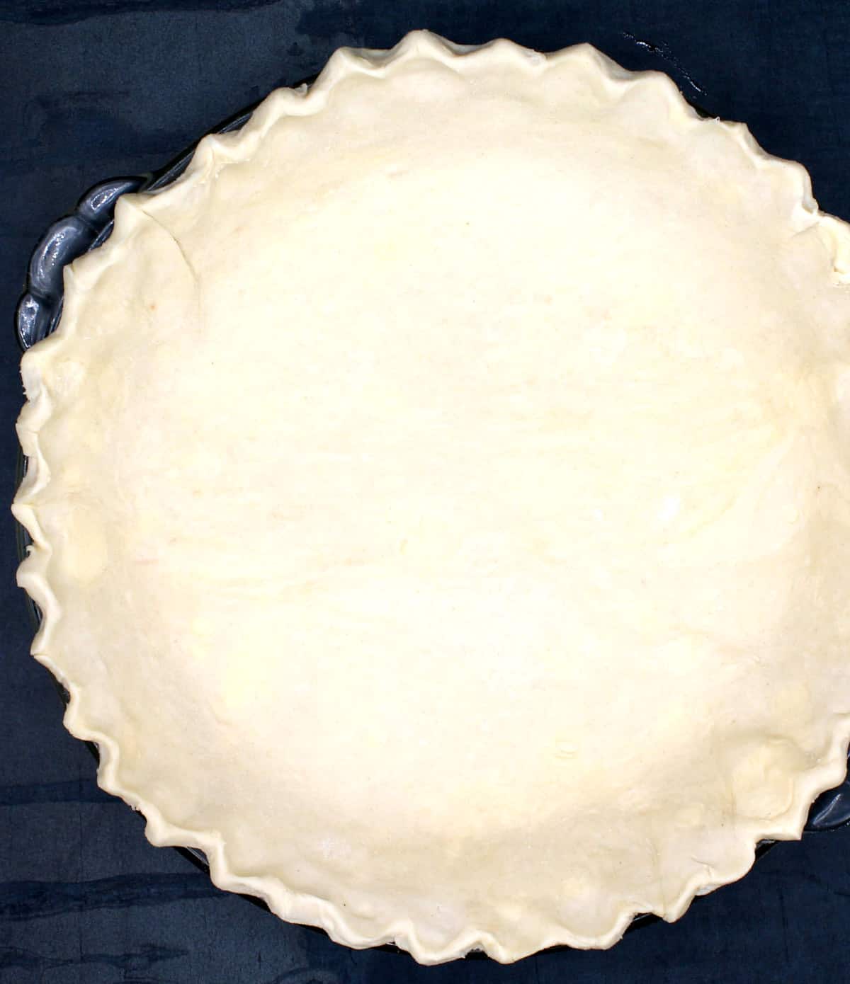 Fluted pie crust in glass pie plate on dark background.