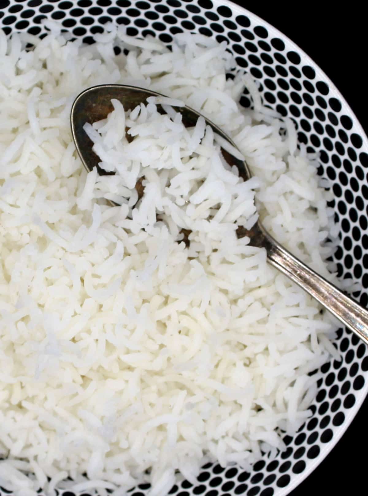 Long grains of cooked basmati rice in black and white bowl with spoon.