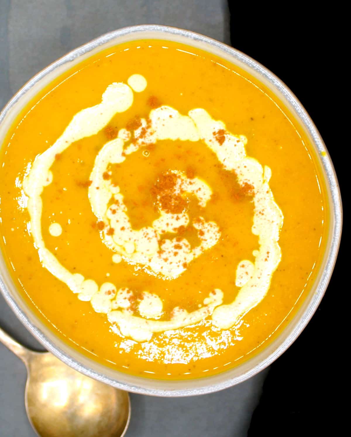 Easy butternut squash soup with ginger, carrots and pumpkin cream in bowl with soup spoon.