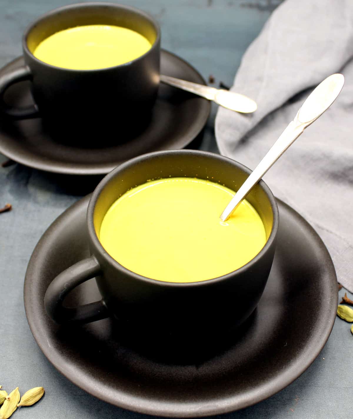 Golden milk made with oat milk and spices in cups and saucers with spoons.