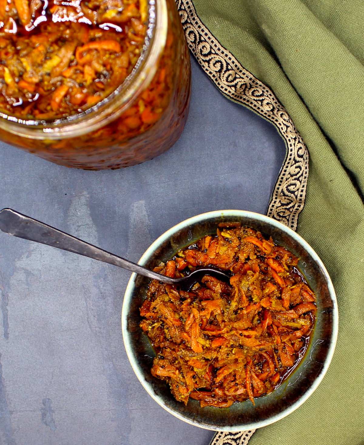 A bowl of gajar ka achar with a jar of the pickled carrots in background.