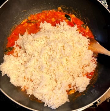 Rice added to tomatoes and spices in wok.