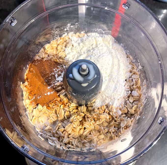 Oats, cinnamon and other ingredients in food processor bowl.