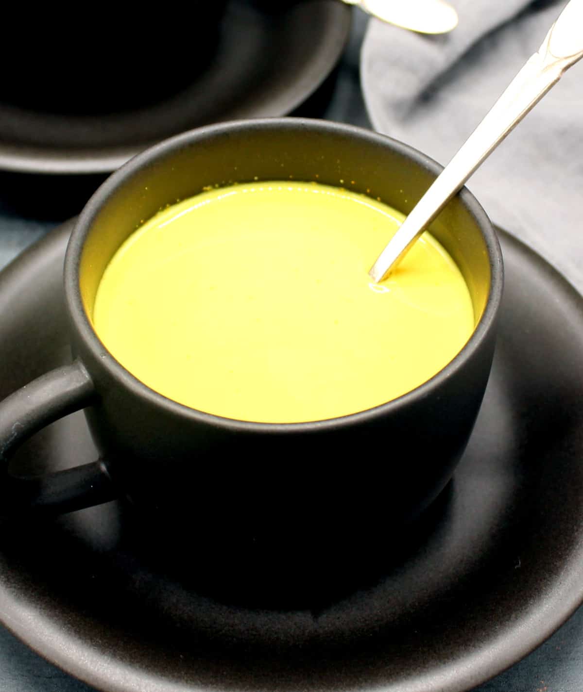 Turmeric milk in black cup with saucer and spoon.