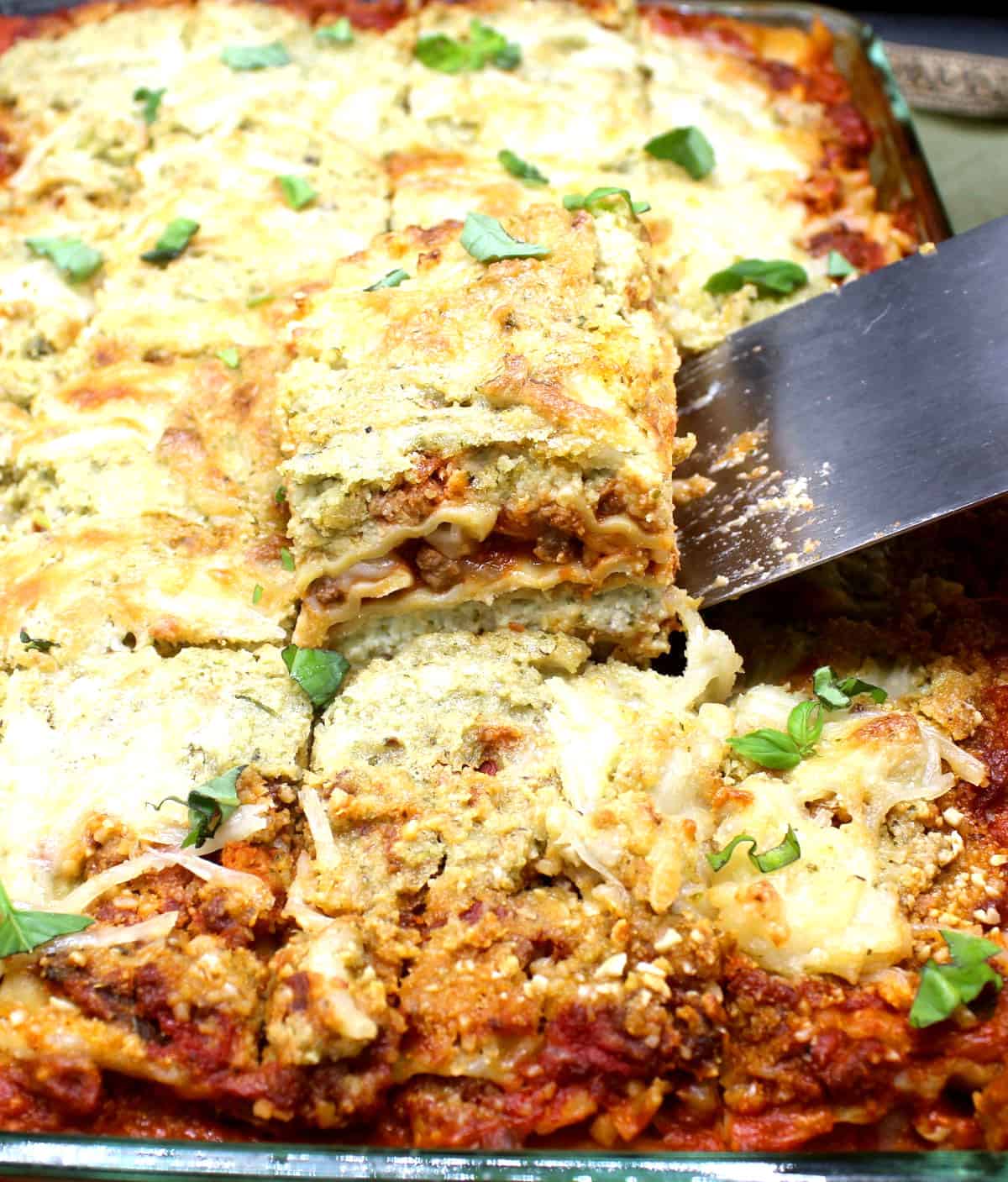 The best vegan lasagna being lifted out of the baking pan with a steel spatula.