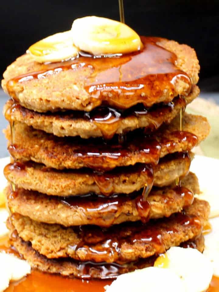 Vegan oatmeal pancakes with banana slices and maple syrup drizzled on top.
