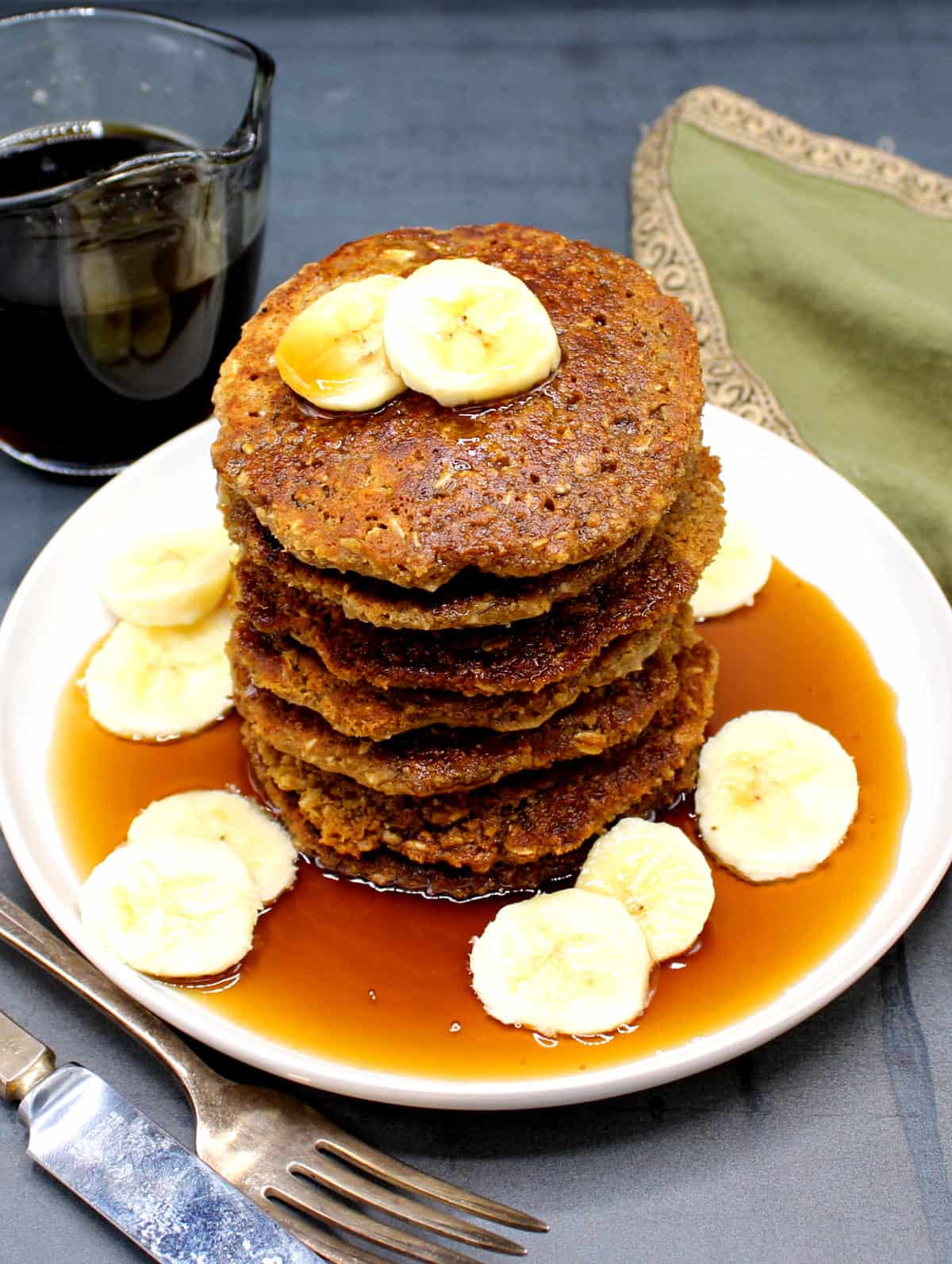 Oatmeal pancakes in plate with maple syrup and banana slices.