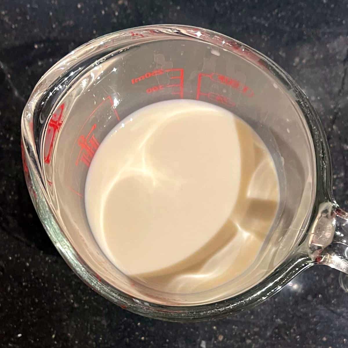 Oat milk mixed with apple cider vinegar in glass measuring cup.