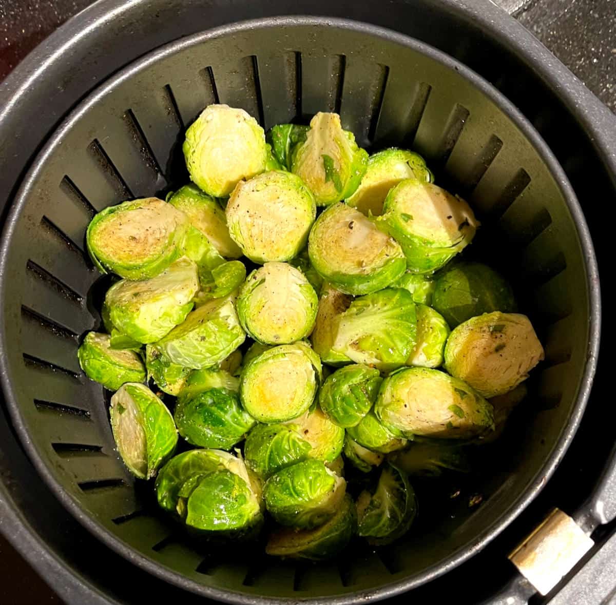Seasoned Brussels sprouts in air fryer basket.