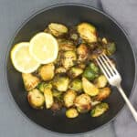 Air fryer brussels sprouts in bowl with fork and slices of lemon.