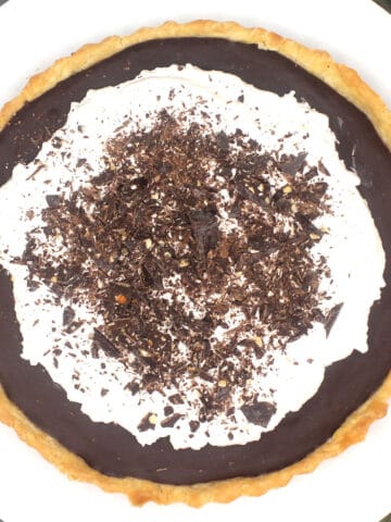 Vegan chocolate pie with mounds of whipped cream topping and shards of dark chocolate.
