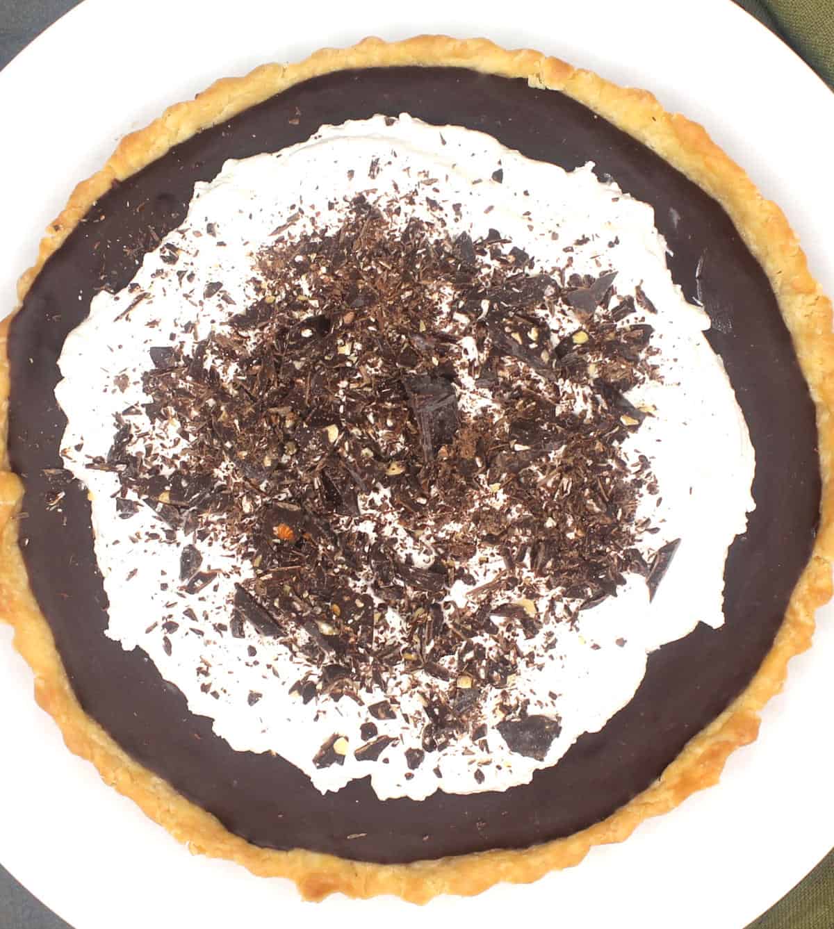 Vegan chocolate pie with mounds of whipped cream topping and shards of dark chocolate.