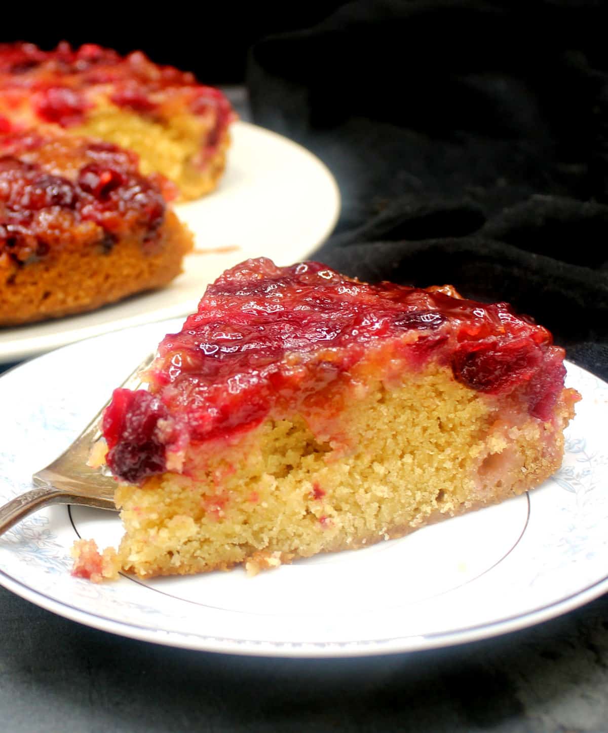Slice of vegan cranberry upside down cake in white plate with fork.