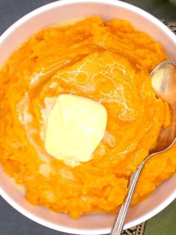 Vegan mashed sweet potatoes in bowl with pat of vegan butter and spoon.