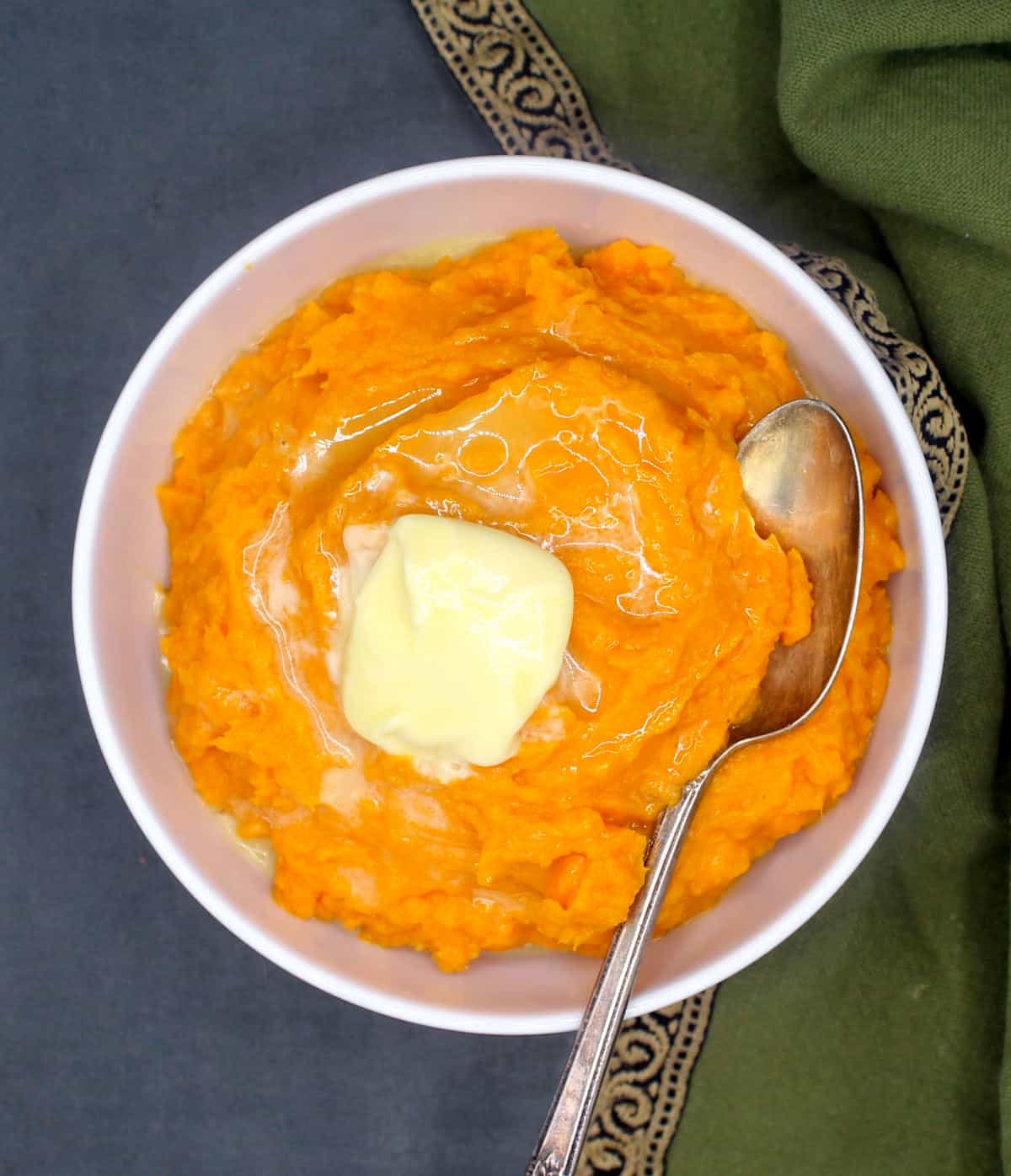 Vegan sweet mashed potatoes with a pat of butter and spoon in bowl.
