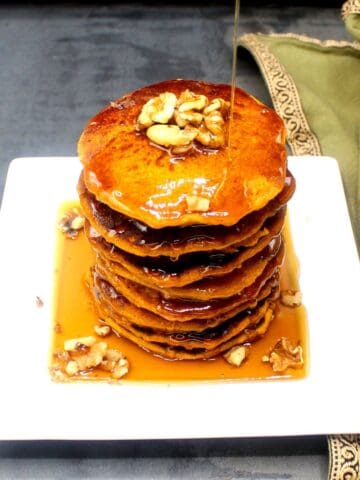 Vegan pumpkin pancakes on square white plate with walnuts and maple syrup.