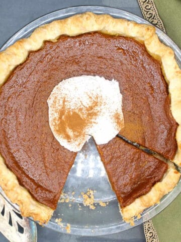 Vegan pumpkin pie with a slice cut out and topped with vegan whipping cream.