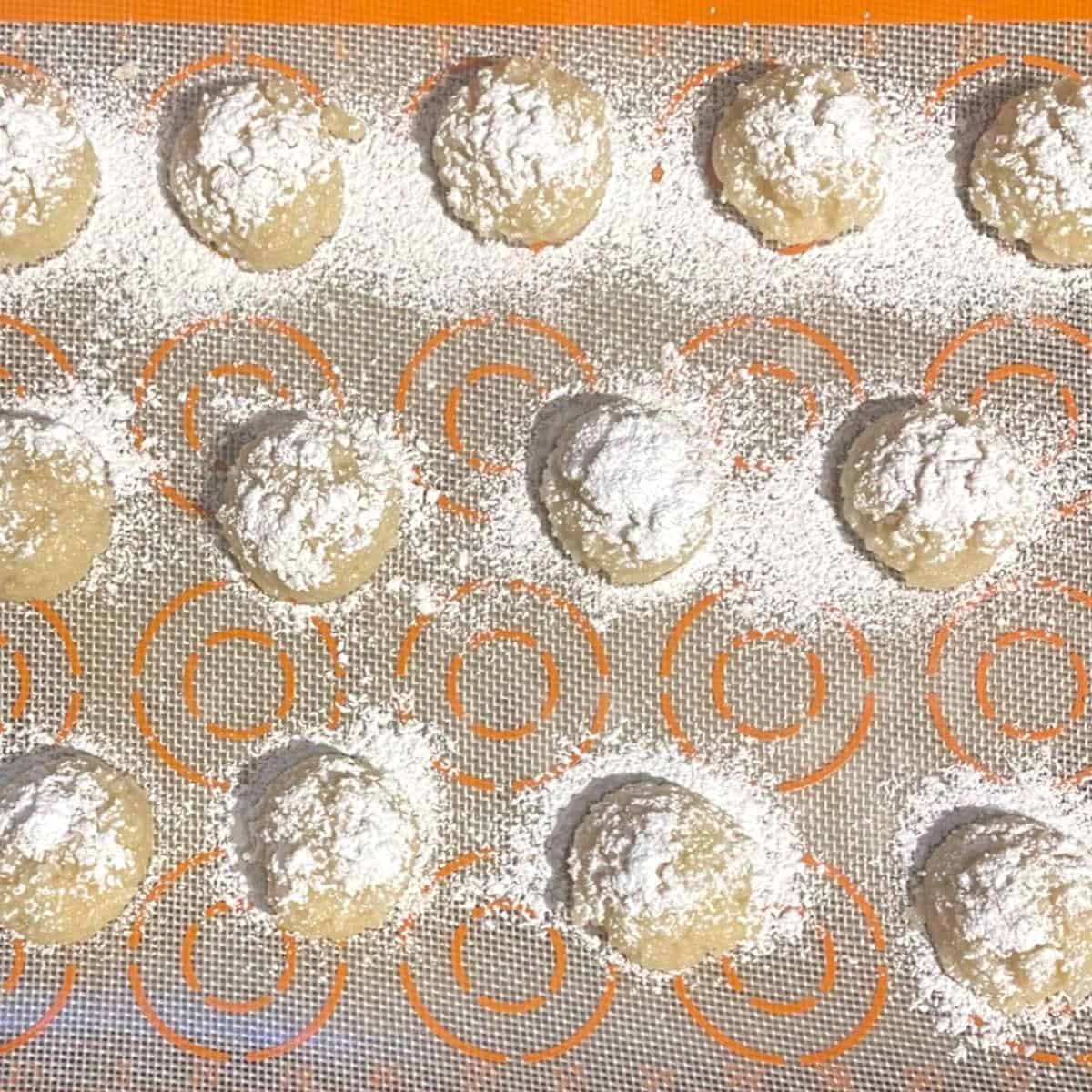 Vegan amaretti cookie dough balls on baking sheet dusted with powdered sugar.