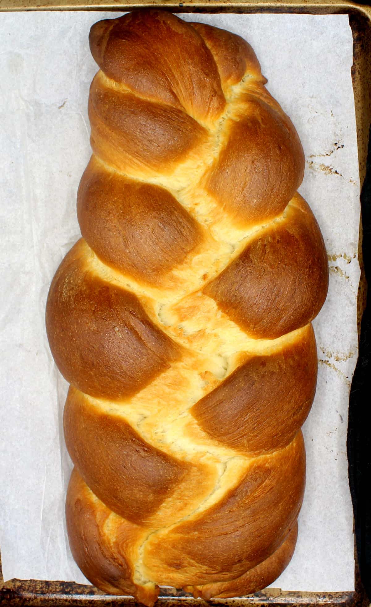 Vegan challah loaf on parchment lined baking pan.