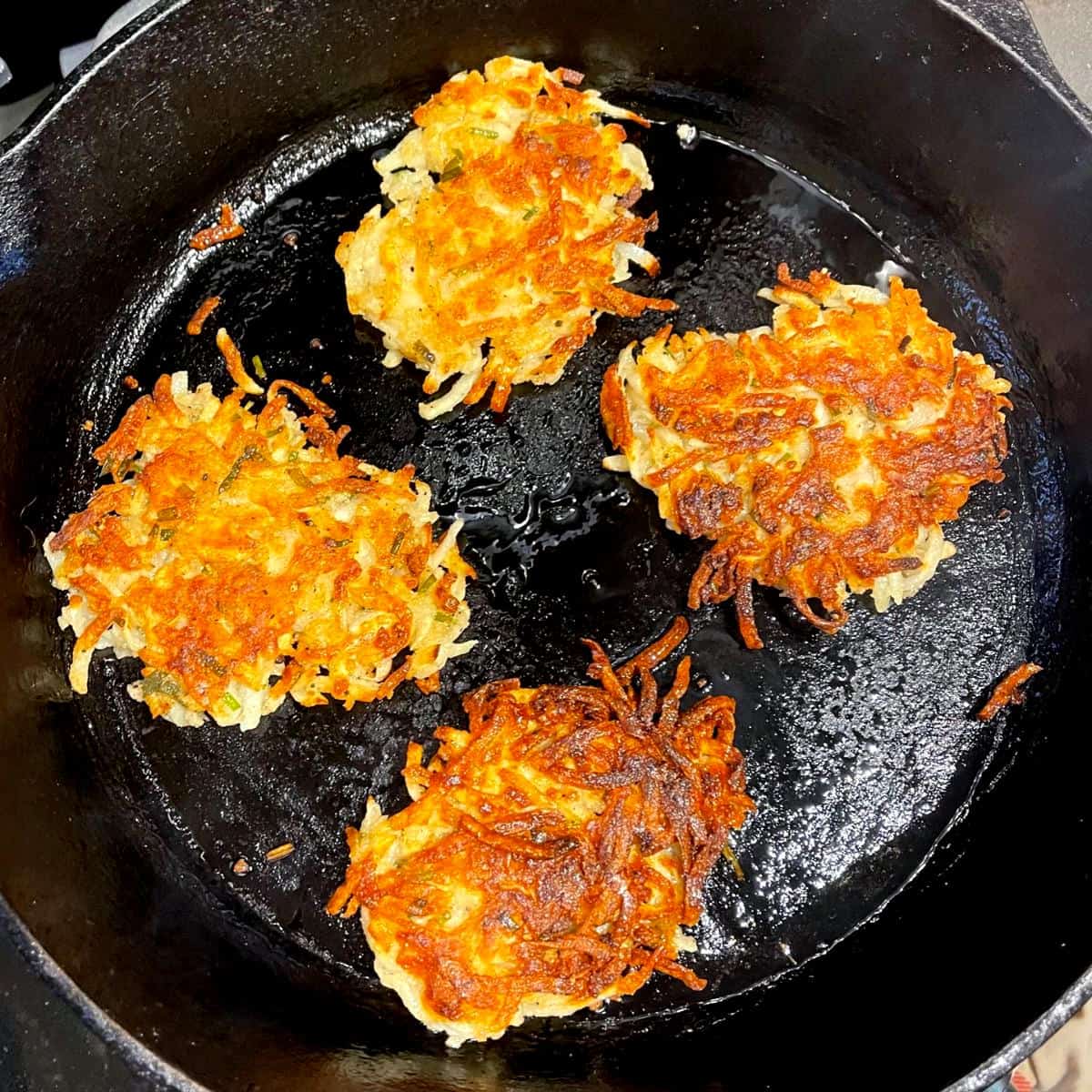 Vegan latkes frying in cast iron pan.