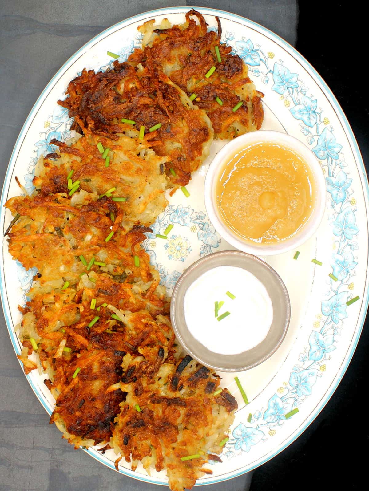 Vegan potato latkes in an oval plate with vegan sour cream and applesauce in bowls.