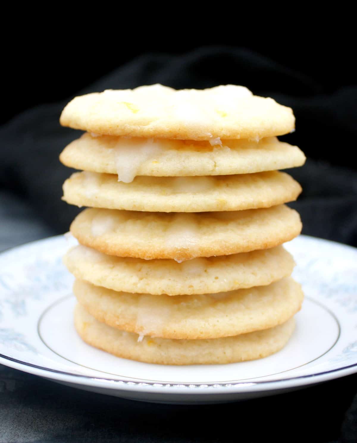Vegan lemon cream cheese cookies stacked on a white and blue china plate.