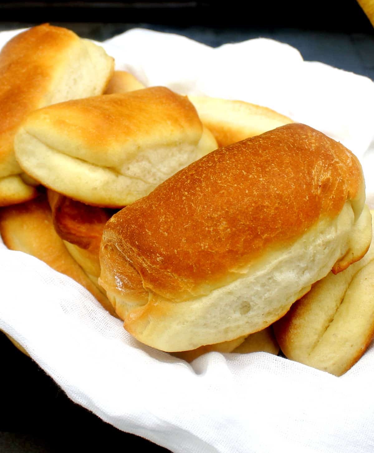 Vegan Parker House rolls nestled in a bread basket lined with a white flour sack cloth.