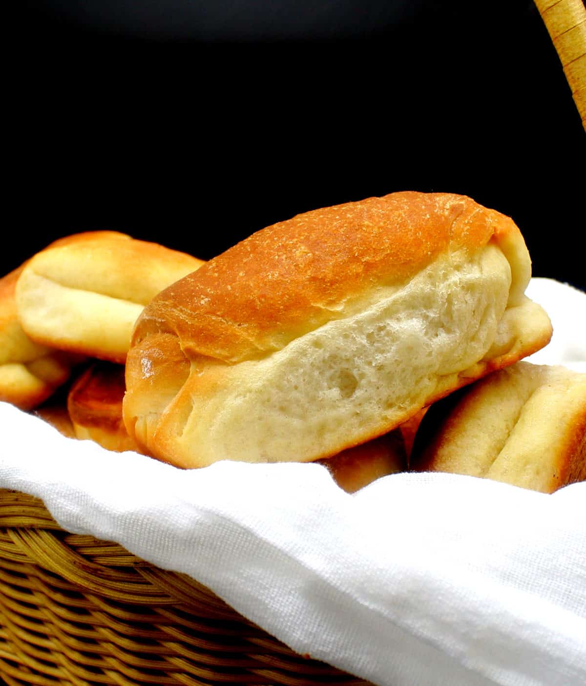 Vegan Parker House rolls nestled in a bread basket lined with a white flour sack cloth.