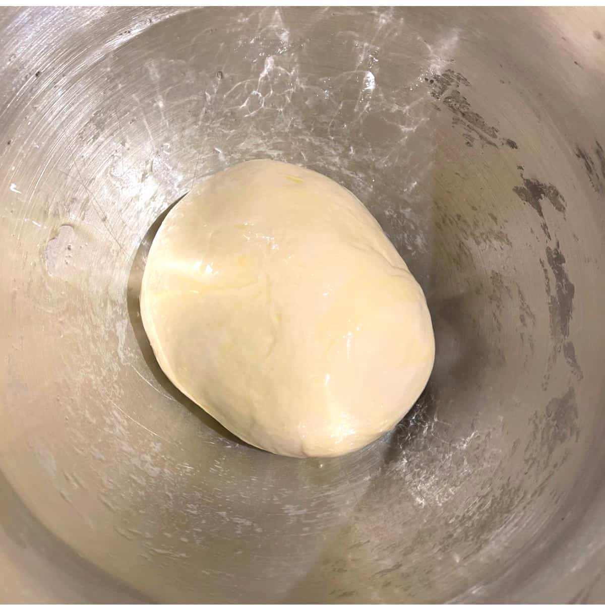 Smooth ball of kneaded dough in oiled bowl.