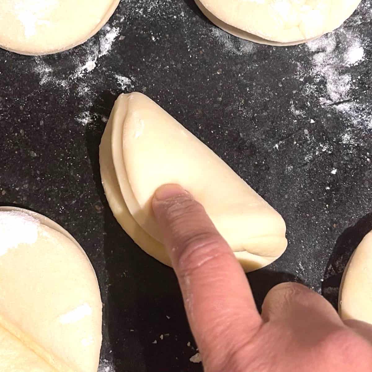 Pressing down on edges of parker house roll with finger.