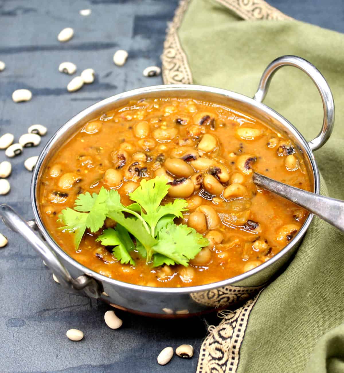 Black eyed peas curry in karahi with cilantro garnish and beans strewn around.