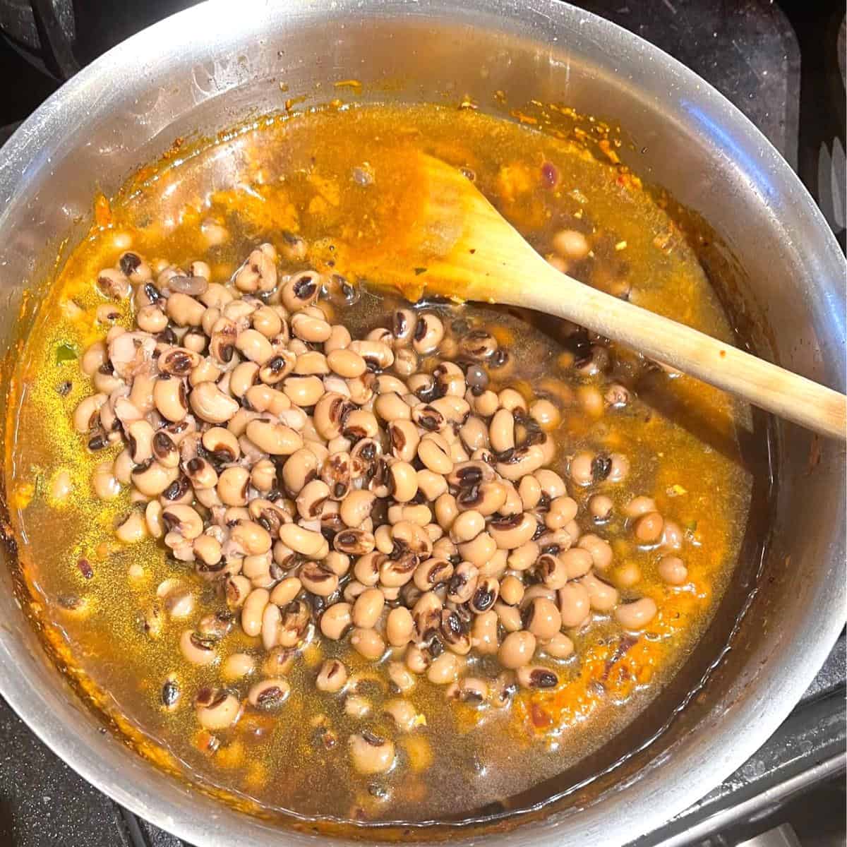 Black eyed peas and stock added to saucepan with masala spices.
