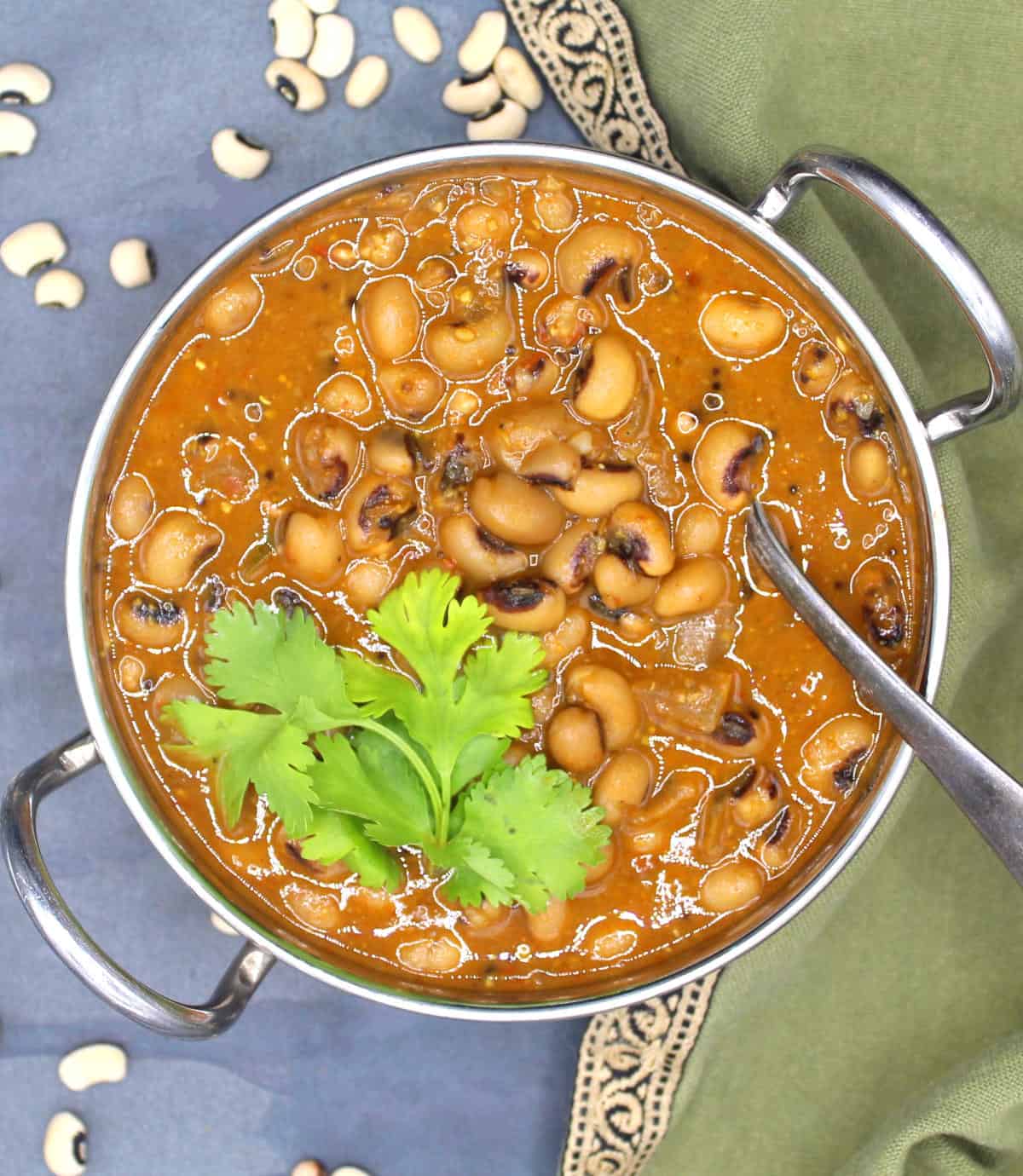 Black-eyed peas curry in karahi with cilantro garnish and beans strewn around.