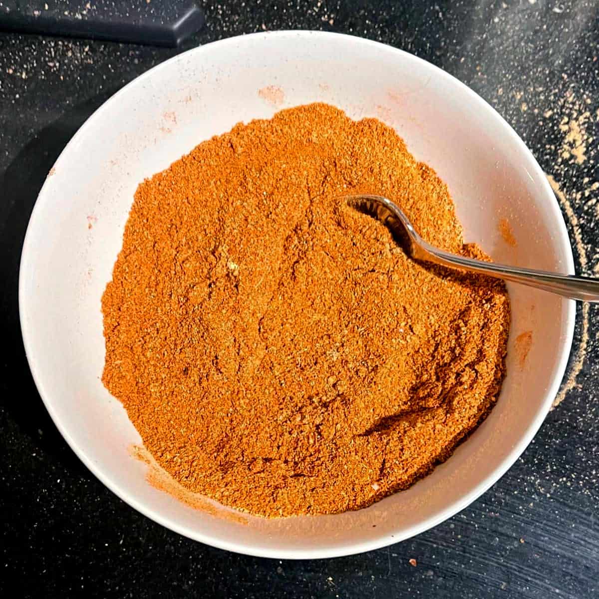 Berbere spice blend in white bowl with spoon.