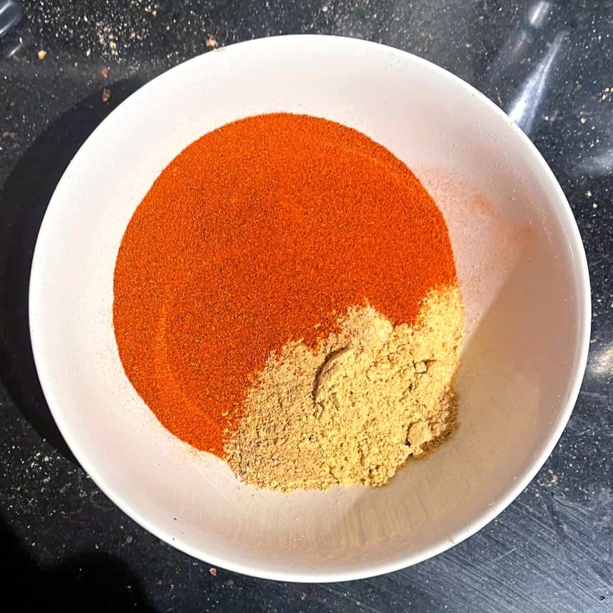 Paprika, ginger and garlic powders added to bowl with blended spices.