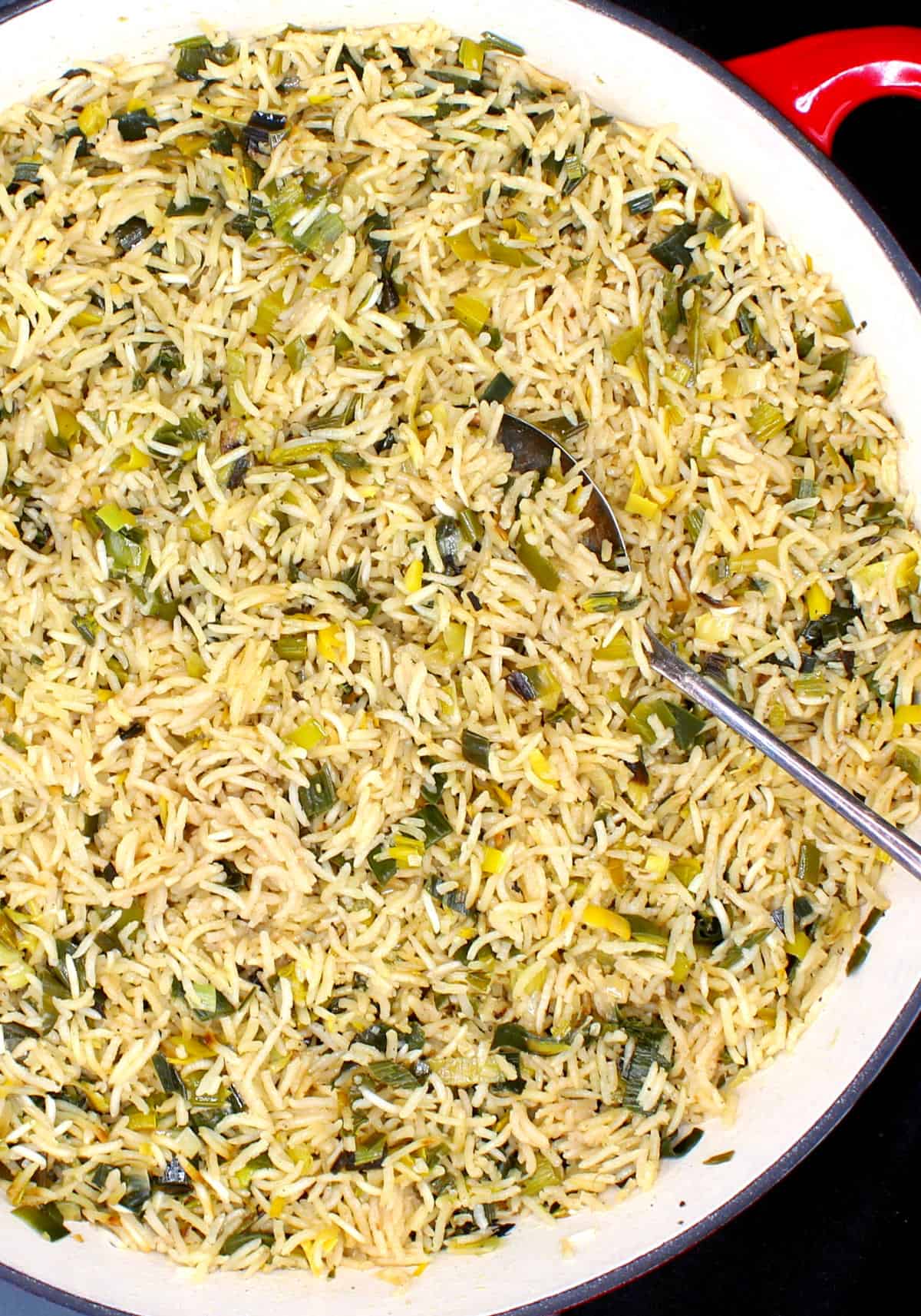 Rice pilaf with leeks in skillet with spoon.