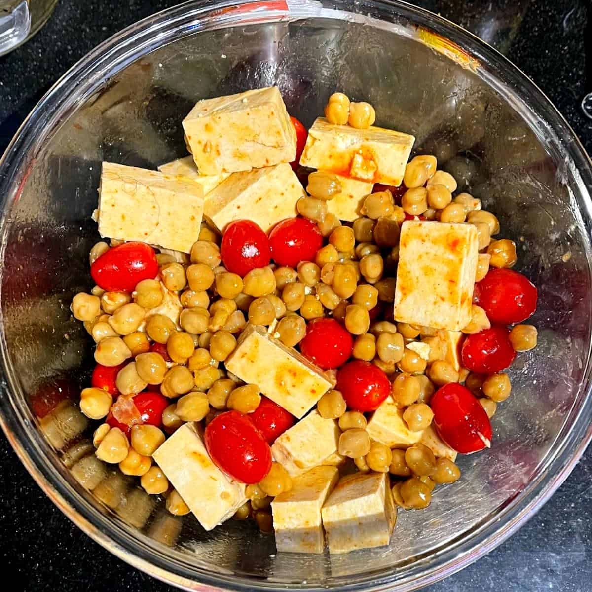 Tofu, chickpeas and cherry tomatoes mixed with sweet and spicy sauce in bowl.