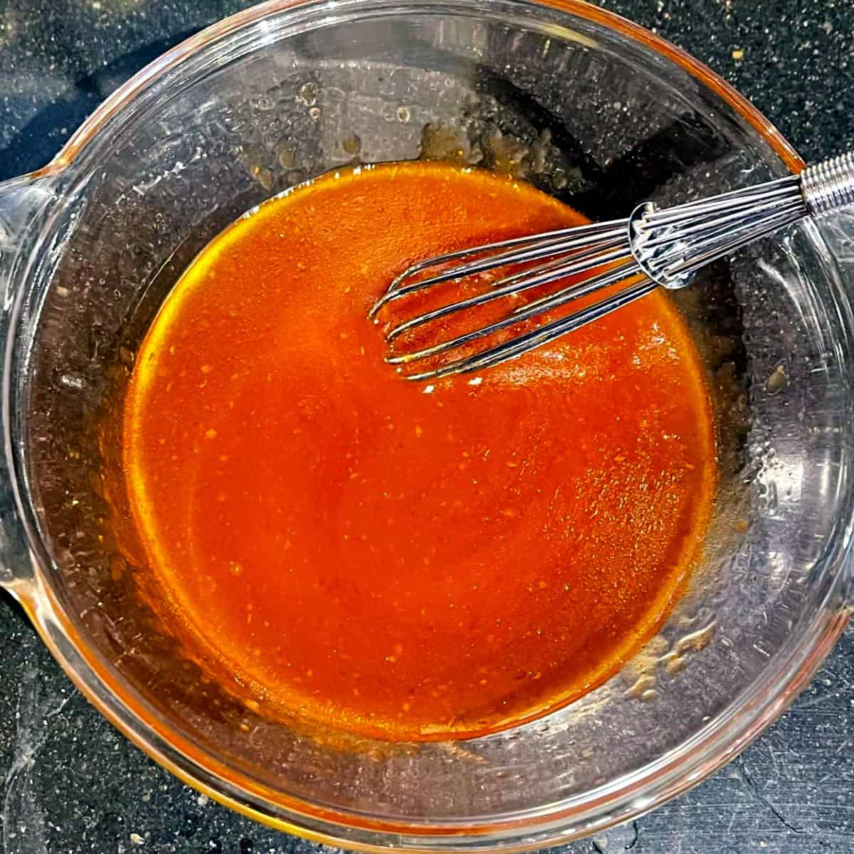 Spicy sweet sauce with maple syrup and sriracha in bowl with whisk.