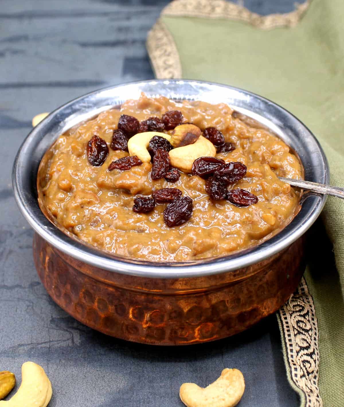 Vegan chakkara pongal in copper and steel bowl with a garnish of cashews and raisins.