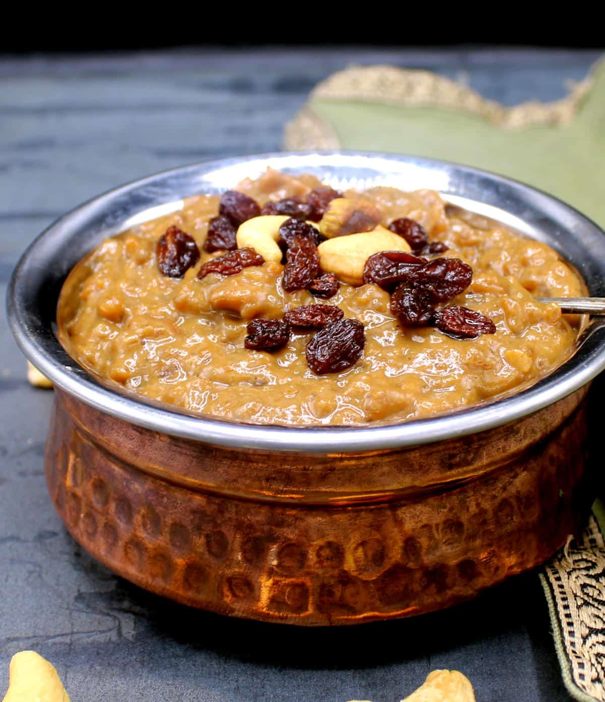 Sweet pongal in copper and steel Indian style bowl with a spoon, and with a nuts and raisins garnish.
