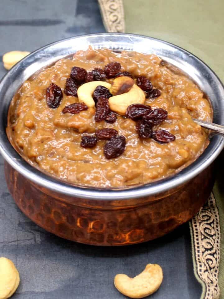 Sakkarai pongal in copper and steel bowl with spoon and with cashews and raisins for garnish.