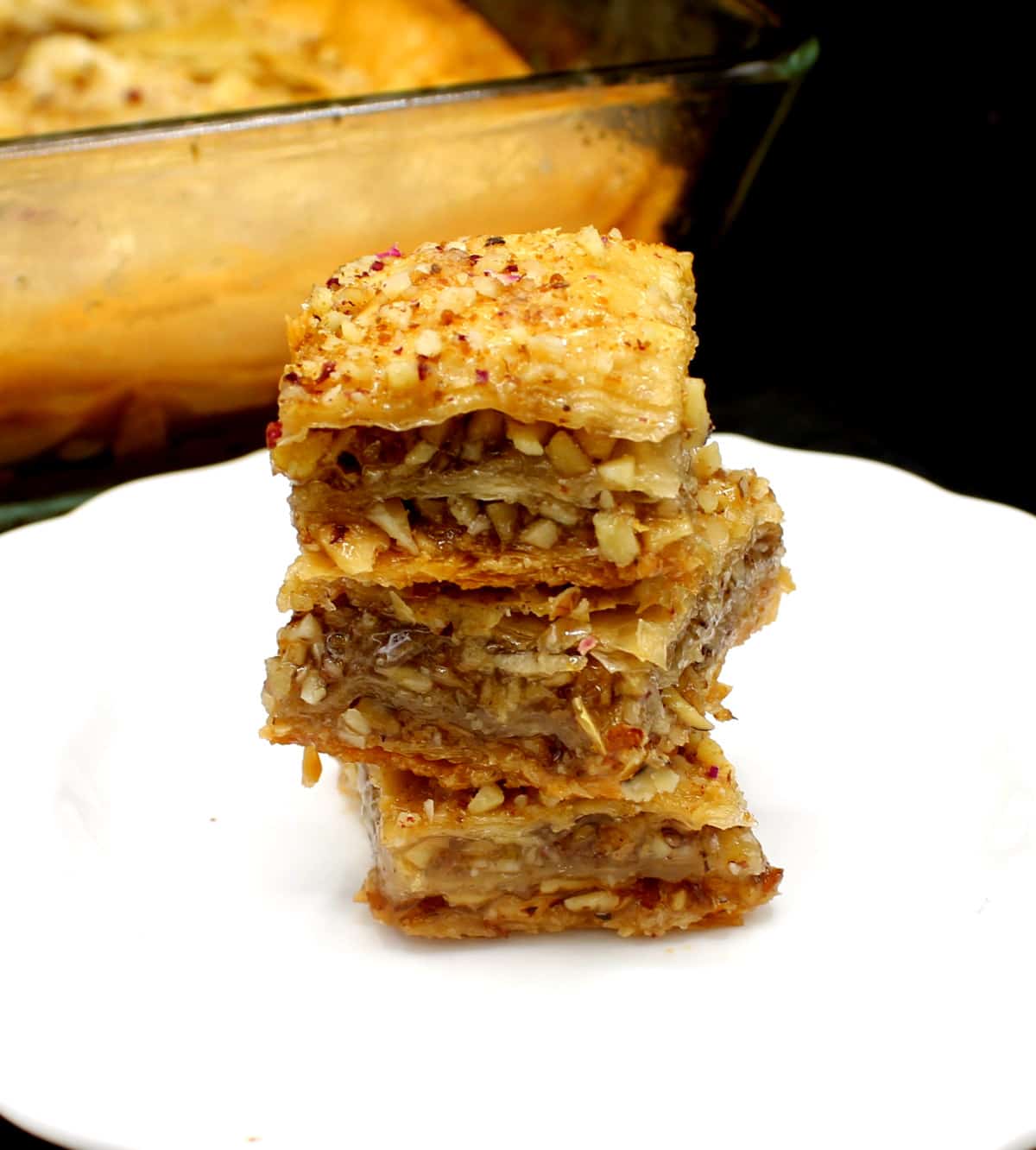 Three pieces of vegan baklava stacked on white plate.