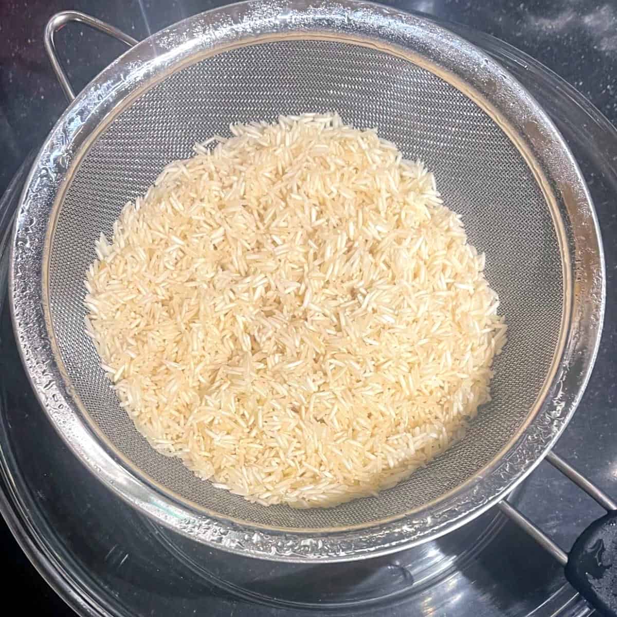Uncooked biryani rice washed and drained in colander.