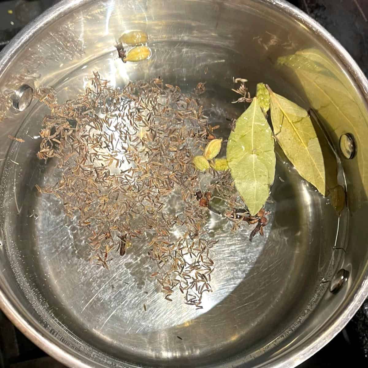 Bay leaves, cardamom, cloves and caraway seeds in water for veg biryani rice.