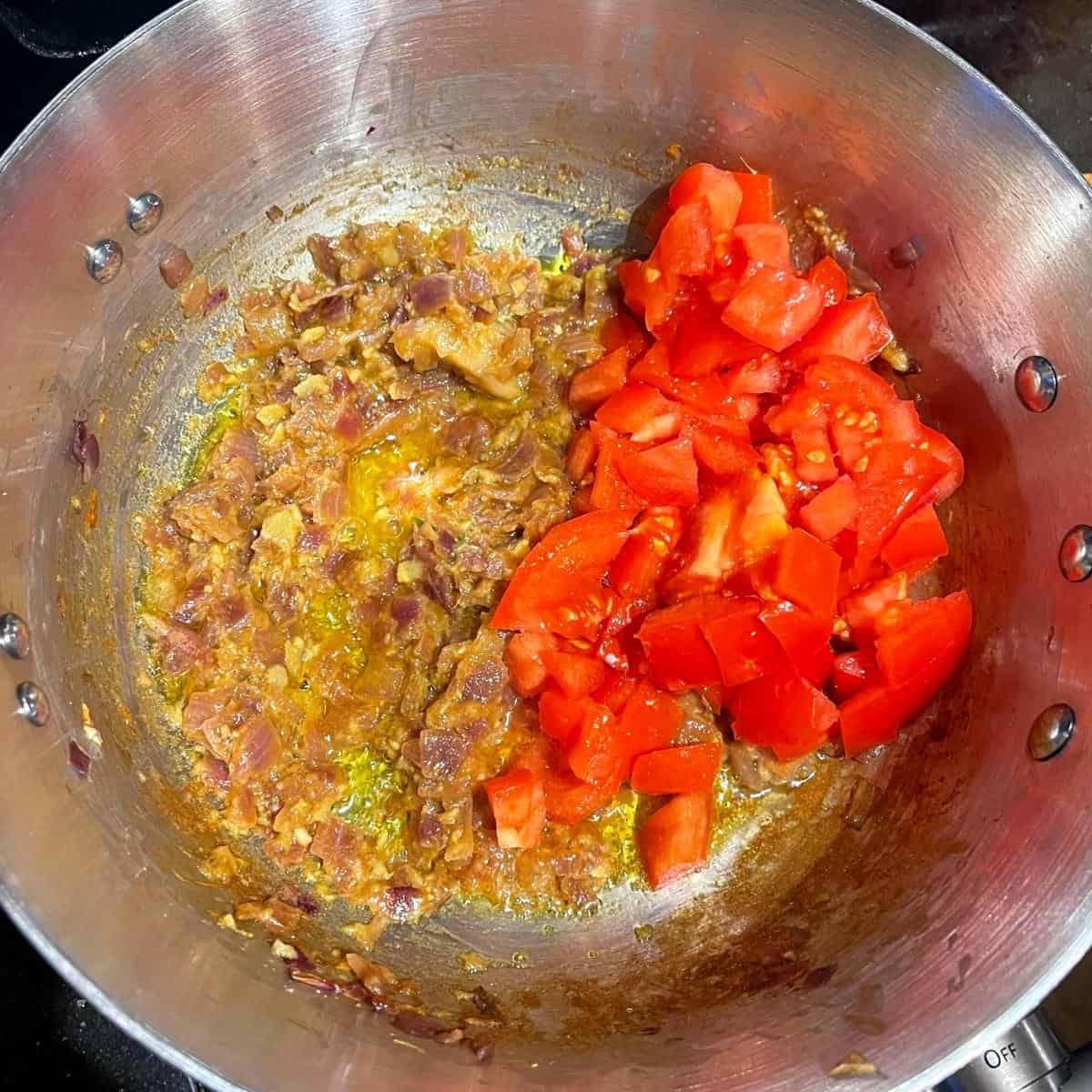 Tomater tillsatta i karamelliserad lök och vitlök i kastrull.