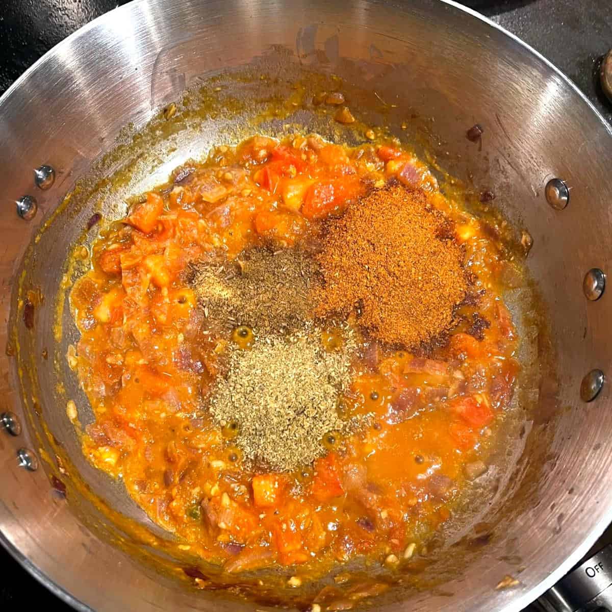 Berbere, coriander powder and cumin powder added to saucepan with tomatoes and onions.