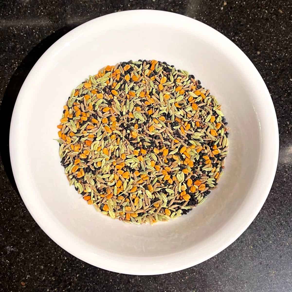 Panch phoron spice blend mixed in white bowl.