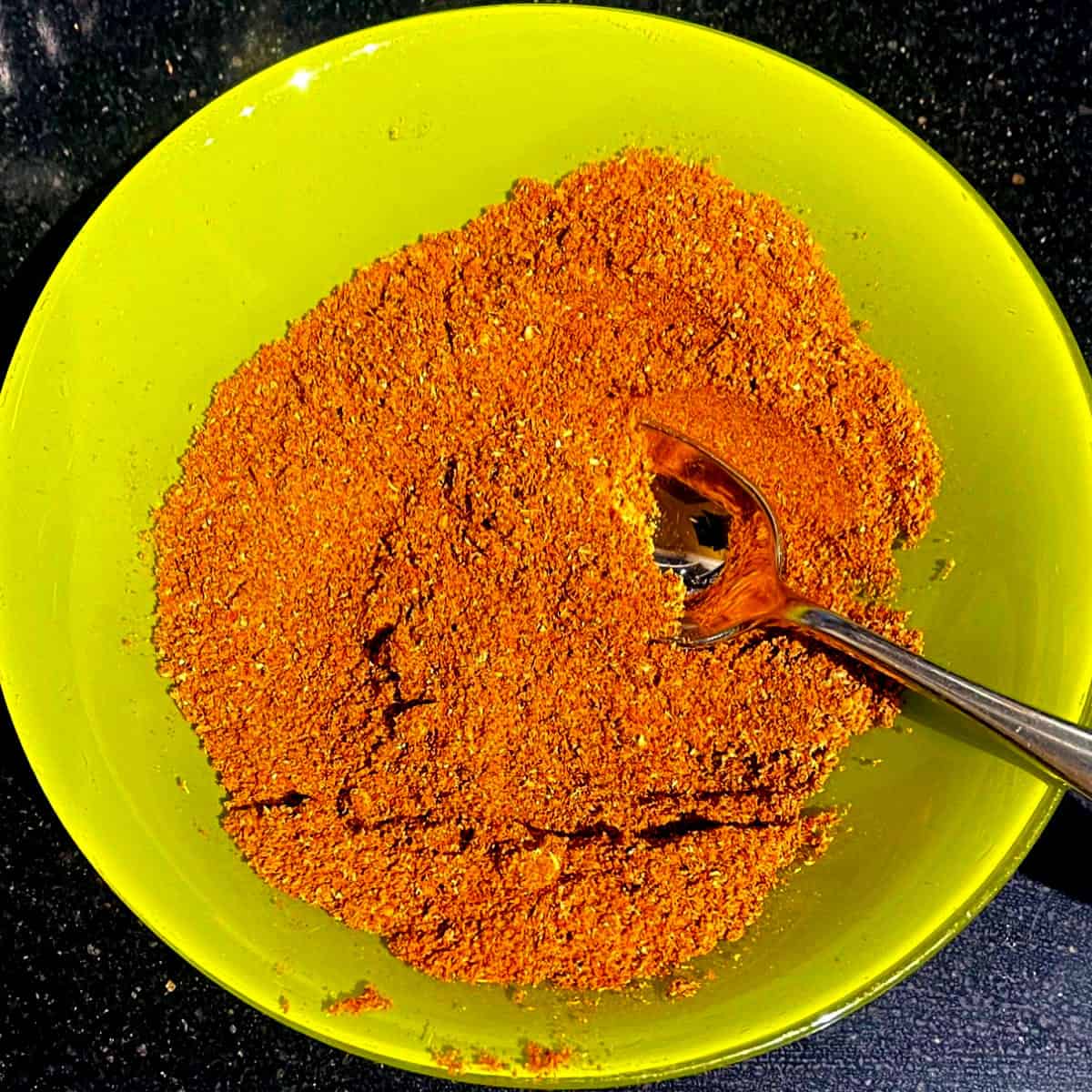 Ras el hanout kryddor blandade i grön skål med sked.