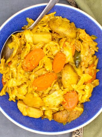 Tikil gomen, Ethiopian cabbage, carrots and potatoes, in blue bowl with spoon.